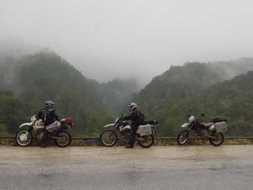 Three motorcycles stopped on a misty mountain road
